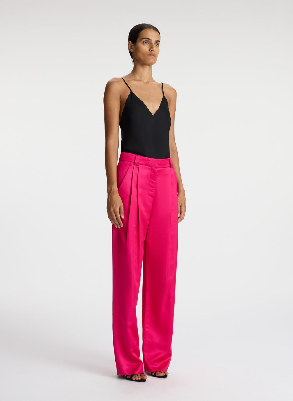 side view of woman wearing black satin camisole with bright pink satin pants