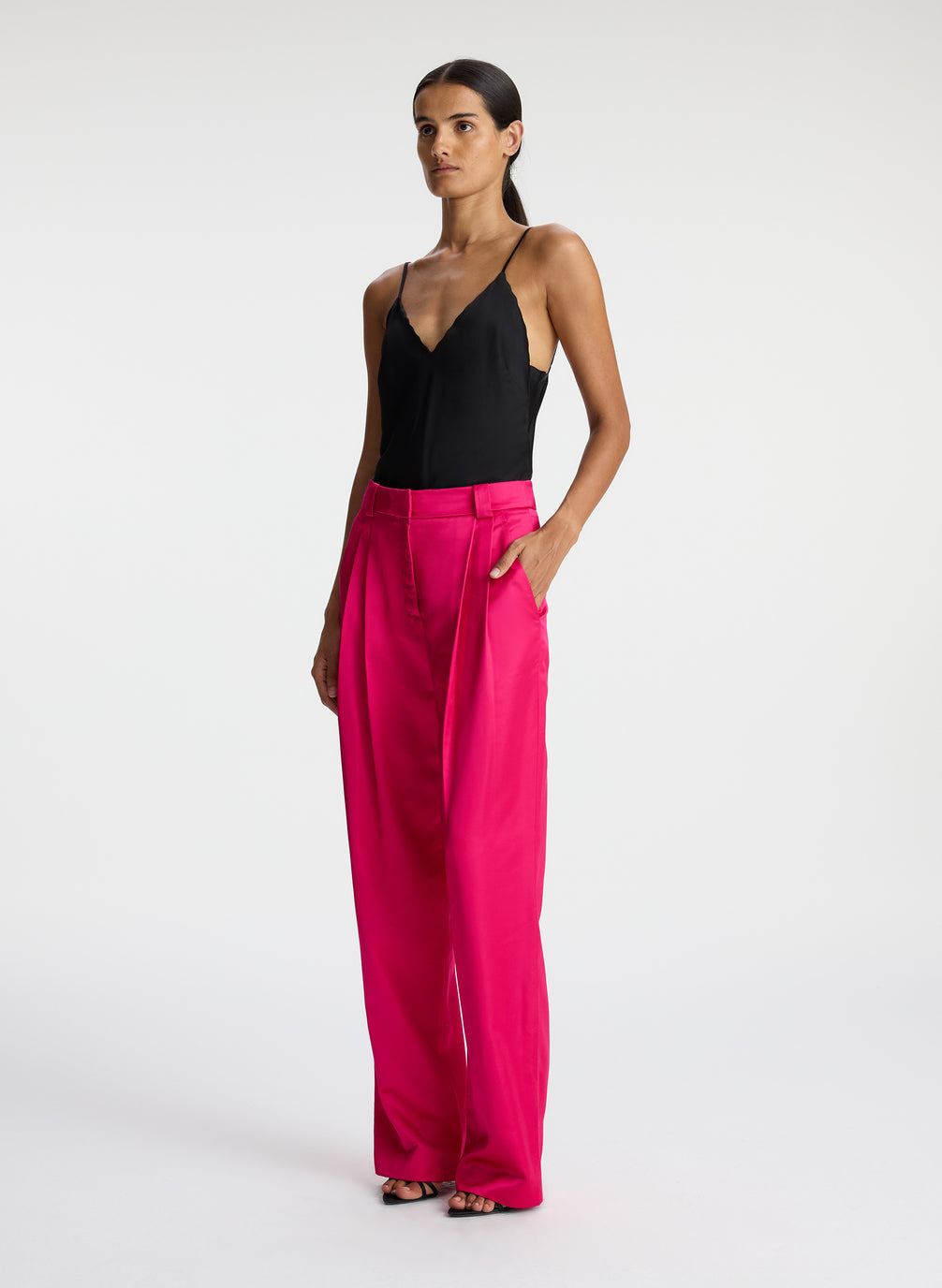 side view of woman wearing black satin camisole with bright pink satin pants