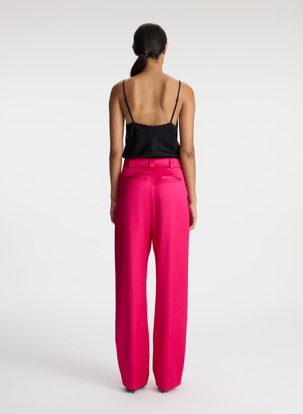 back view of woman wearing black satin camisole with bright pink satin pants