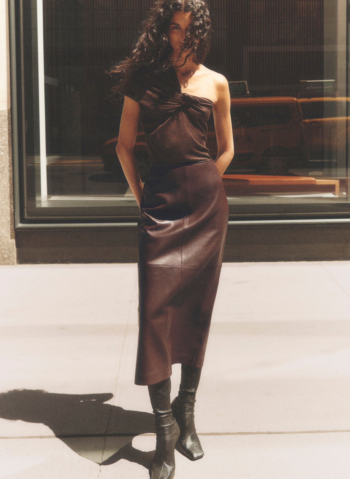 woman wearing bordeaux leather midi skirt and coordinating one shoulder knit top