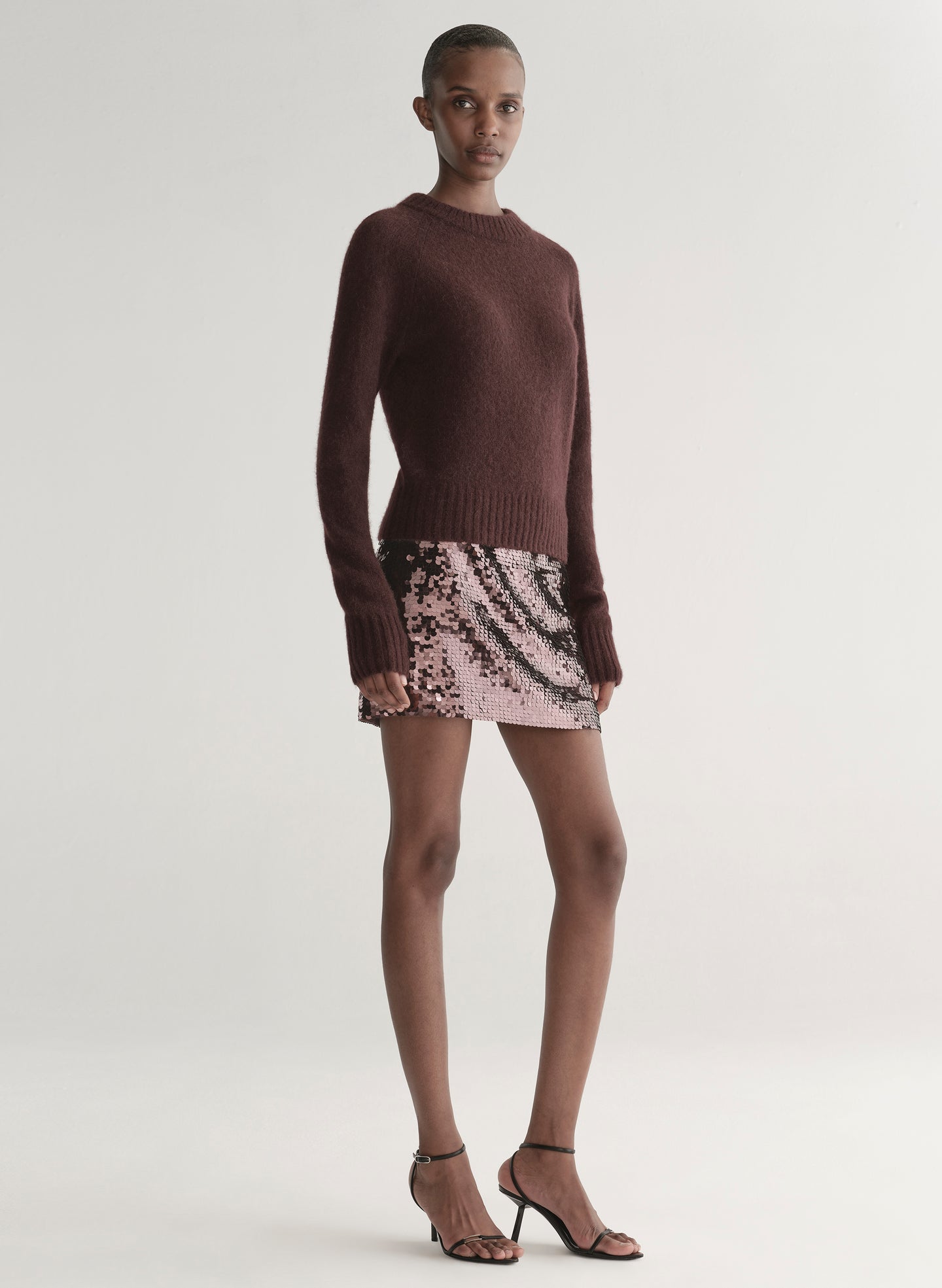 Person wearing a brown sweater and sequin mini skirt on a plain background
