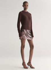 Person wearing a brown sweater and sequin mini skirt on a plain background