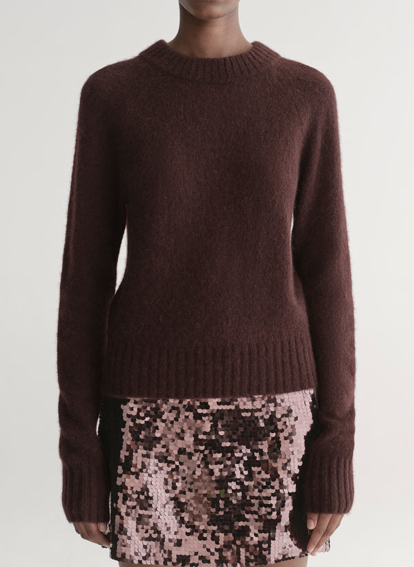 Person wearing a brown sweater and sequin mini skirt on a plain background