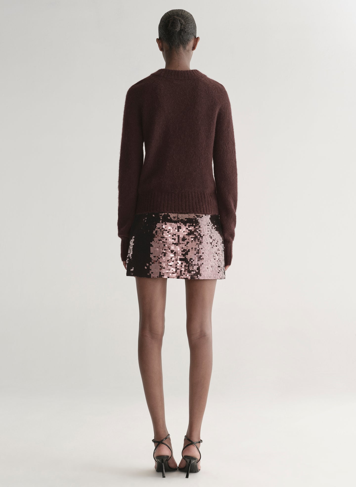 Person wearing a brown sweater and sequin mini skirt on a plain background