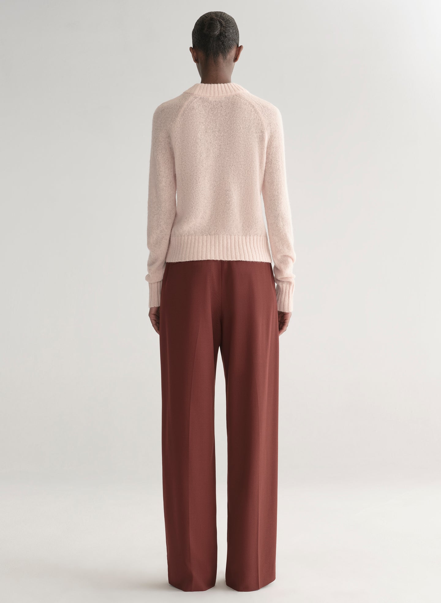 Woman wearing a light pink sweater and maroon pants on a light gray background