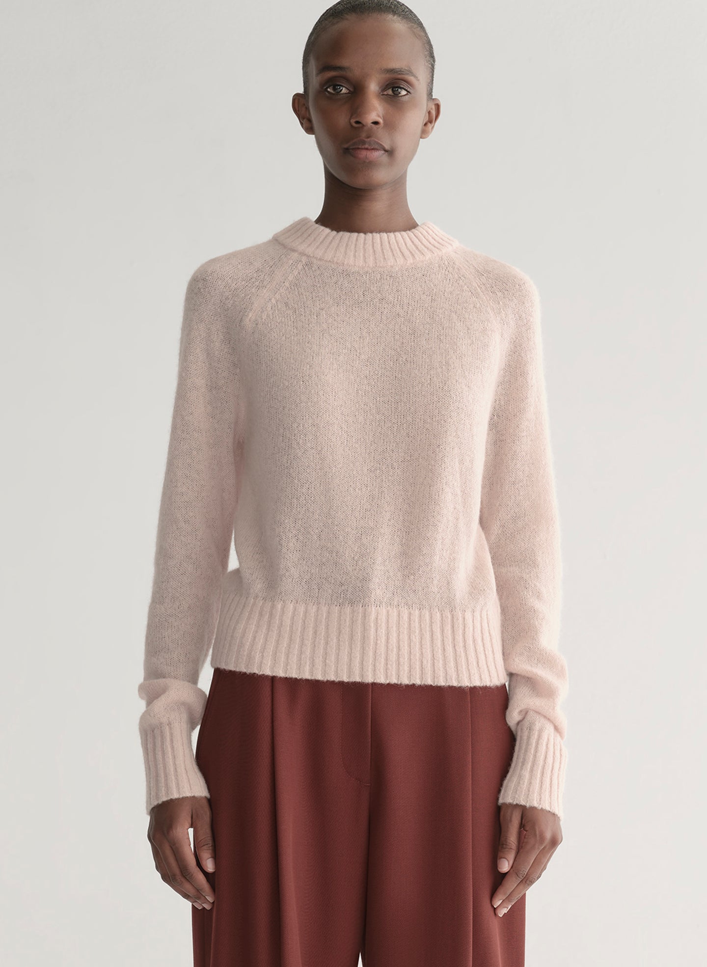 Woman wearing a light pink sweater and maroon pants on a light gray background