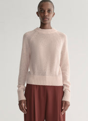 Woman wearing a light pink sweater and maroon pants on a light gray background