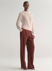 Woman wearing a light pink sweater and maroon pants on a light gray background