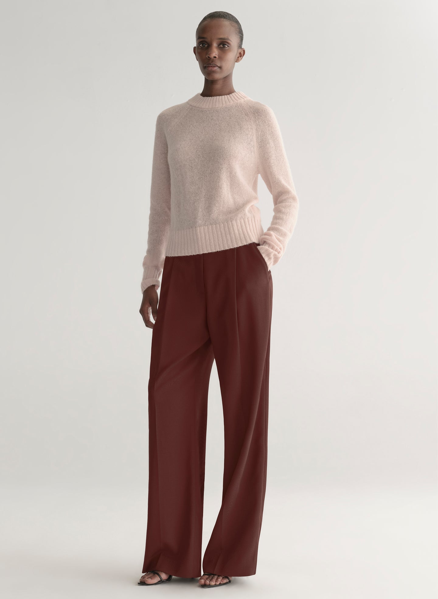 Woman wearing a light pink sweater and maroon pants on a light gray background