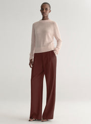 Woman wearing a light pink sweater and maroon pants on a light gray background