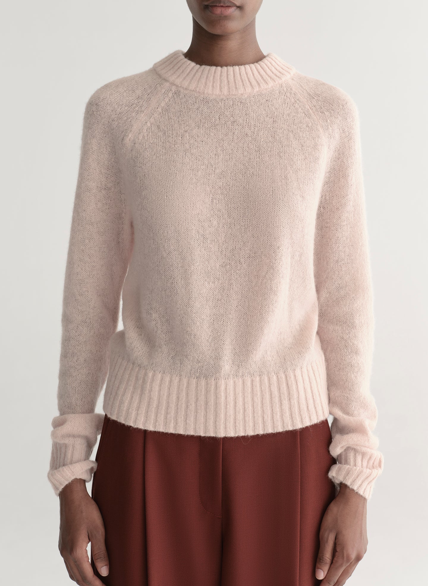 Woman wearing a light pink sweater and maroon pants on a light gray background