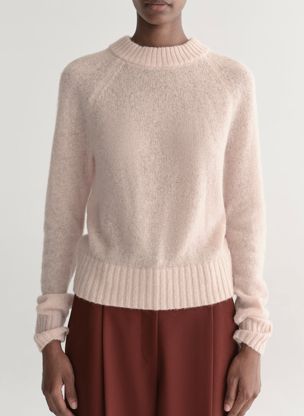 Woman wearing a light pink sweater and maroon pants on a light gray background