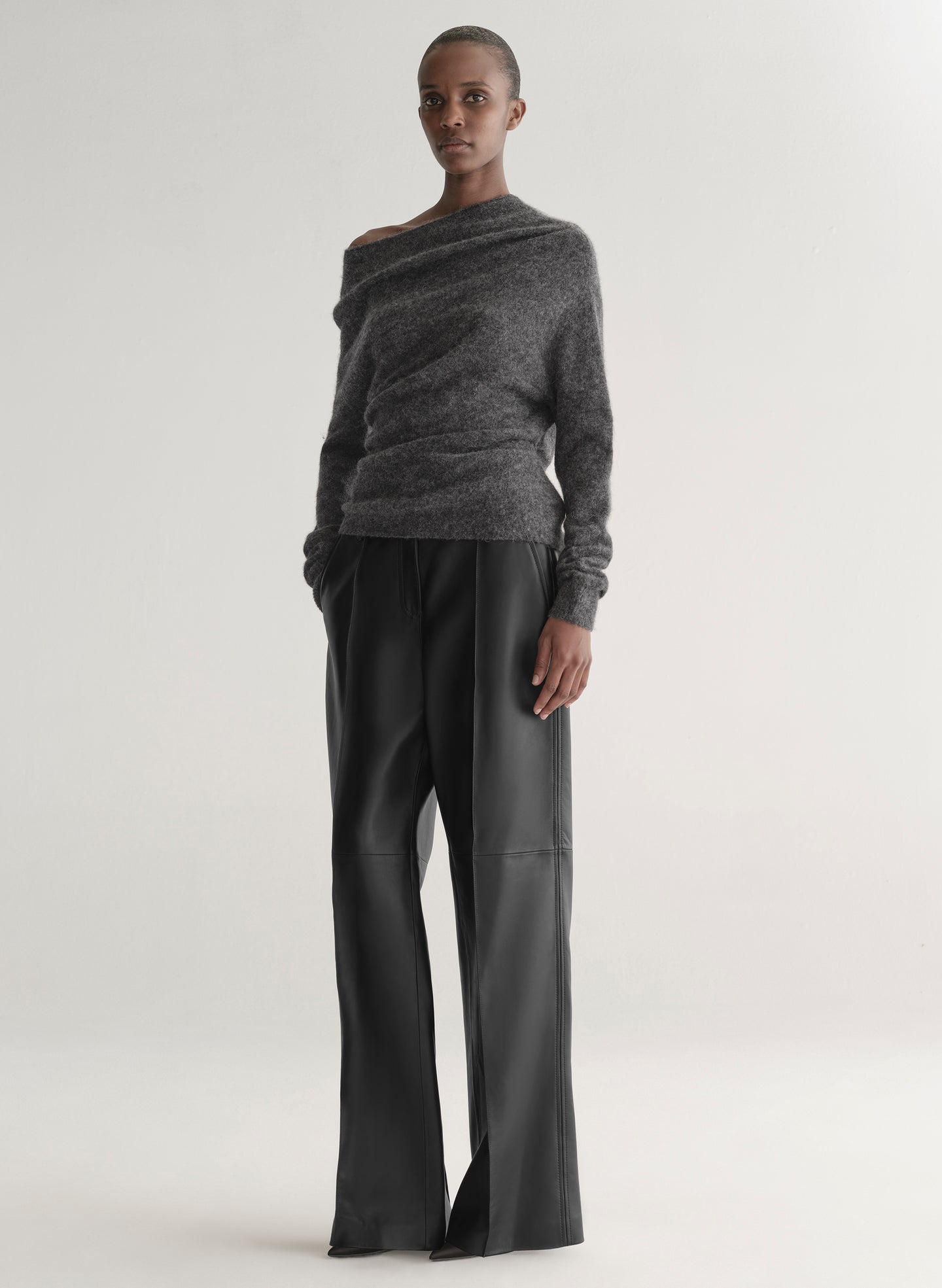 Person wearing a gray off-shoulder sweater and black pants on a white background