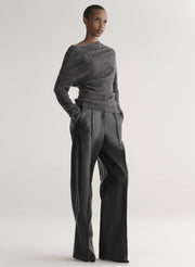 Person wearing a gray sweater and dark pants on a light gray background