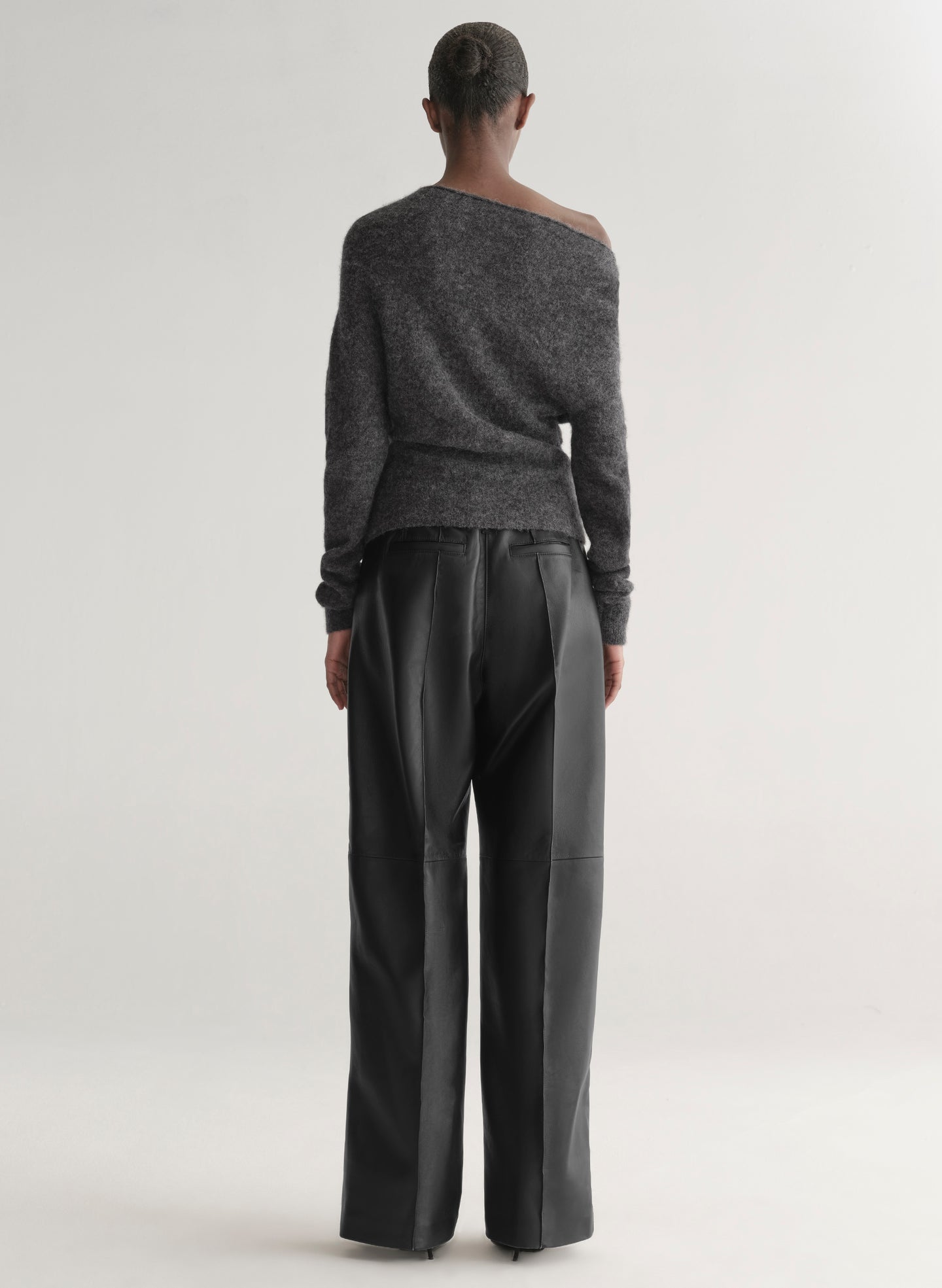 Person wearing a gray off-shoulder sweater and black pants on a white background