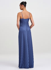 A woman modeling a floor-length pleated blue gown from the back, shown against a plain light gray studio background.