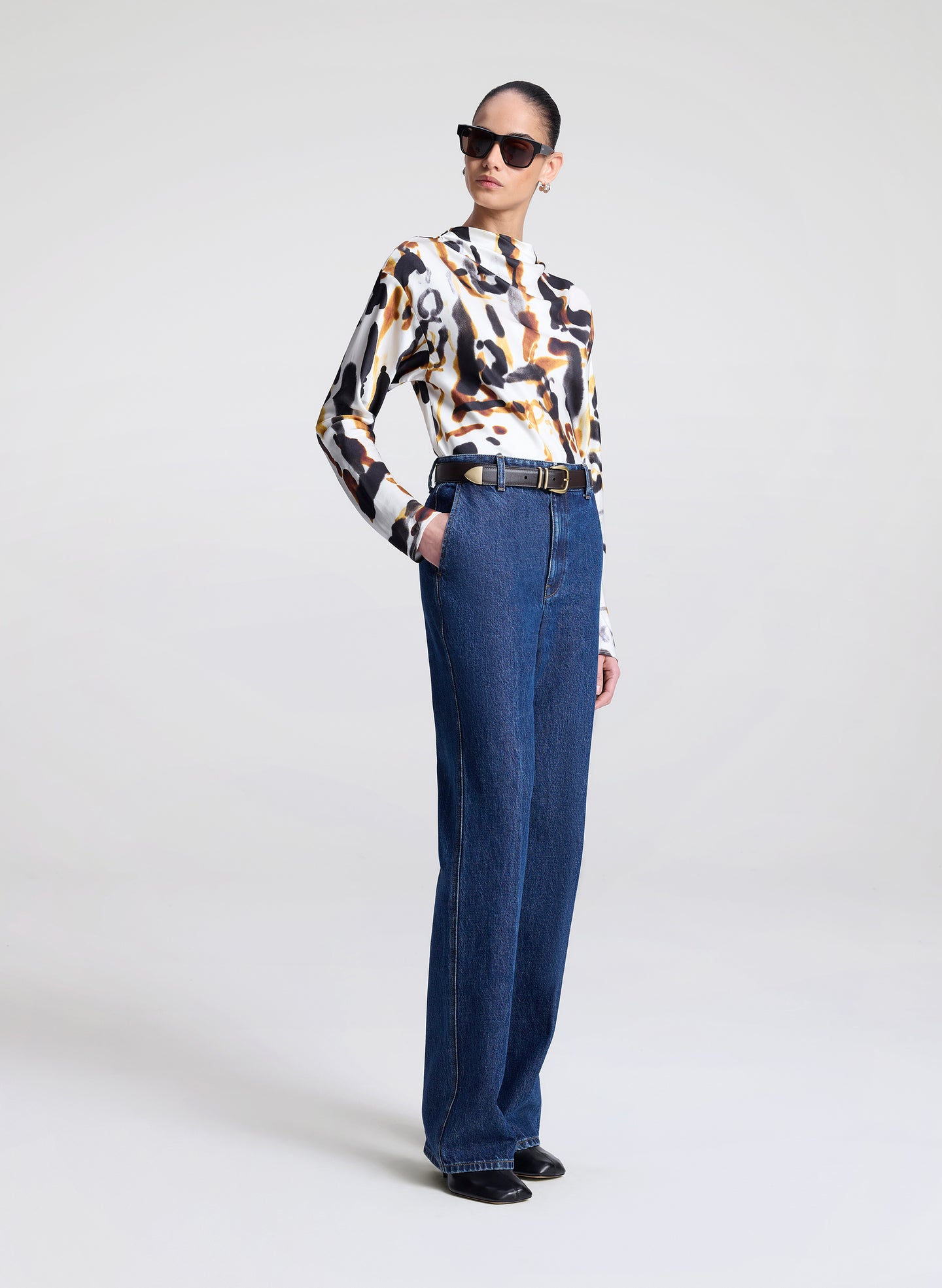 Person wearing a patterned blouse and blue jeans on a white background