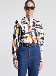 Person wearing a patterned blouse and blue jeans on a plain background