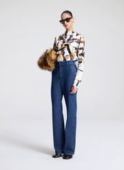 Person wearing a patterned shirt, blue jeans, and sunglasses on a white background