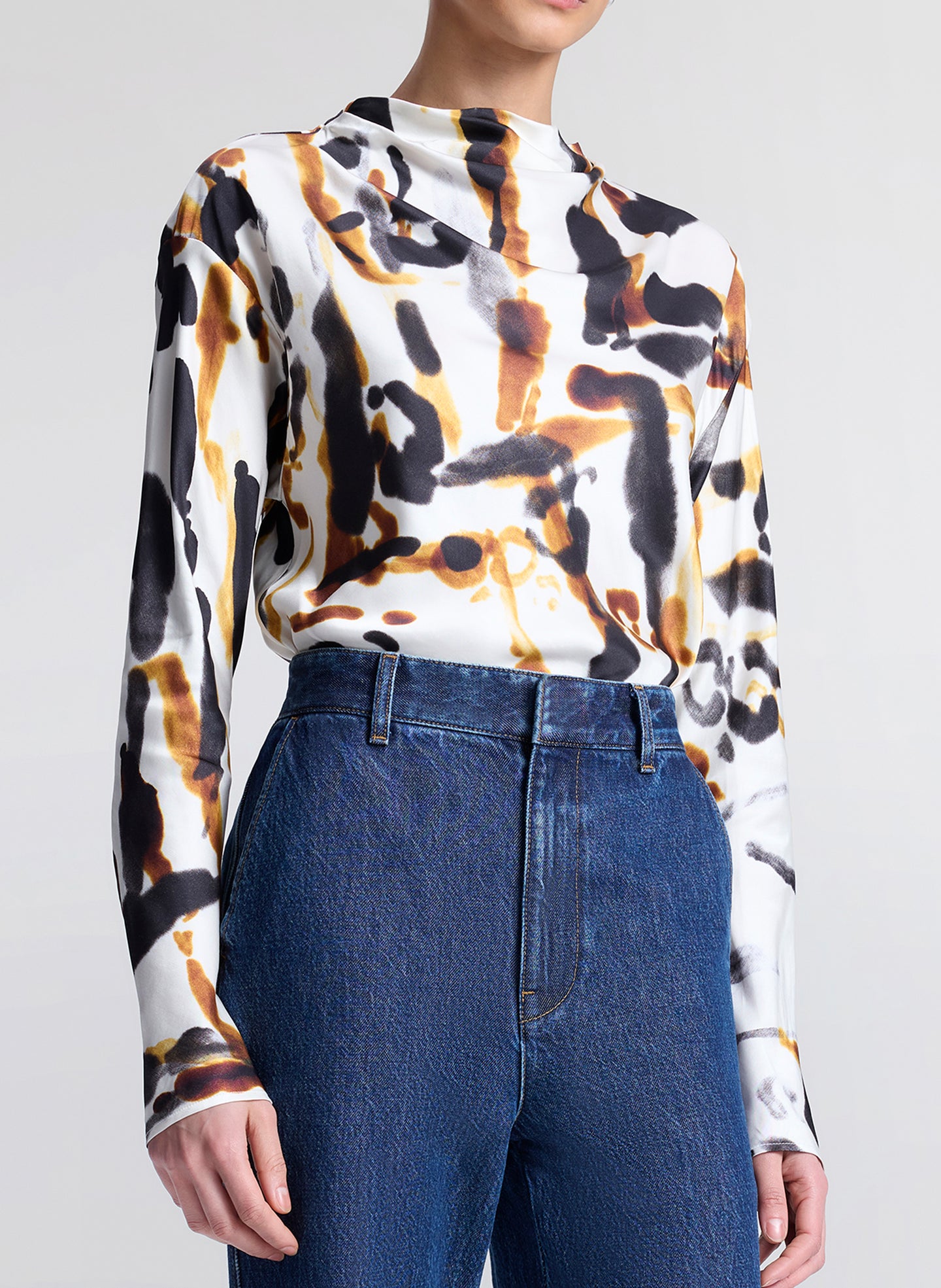 Person wearing a long-sleeve top with a abstract pattern and blue jeans on a light gray background