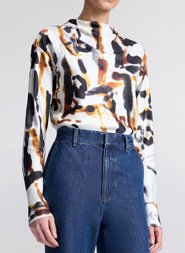 Person wearing a long-sleeve top with a abstract pattern and blue jeans on a light gray background