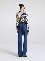 Person wearing a patterned top and blue jeans on a white background