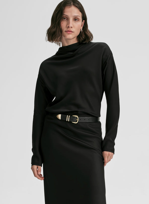 Woman wearing a black long-sleeve top and black skirt with a belt on a light gray background