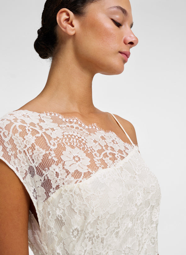 Close-up side profile of a woman wearing a white lace gown against a plain light gray background.