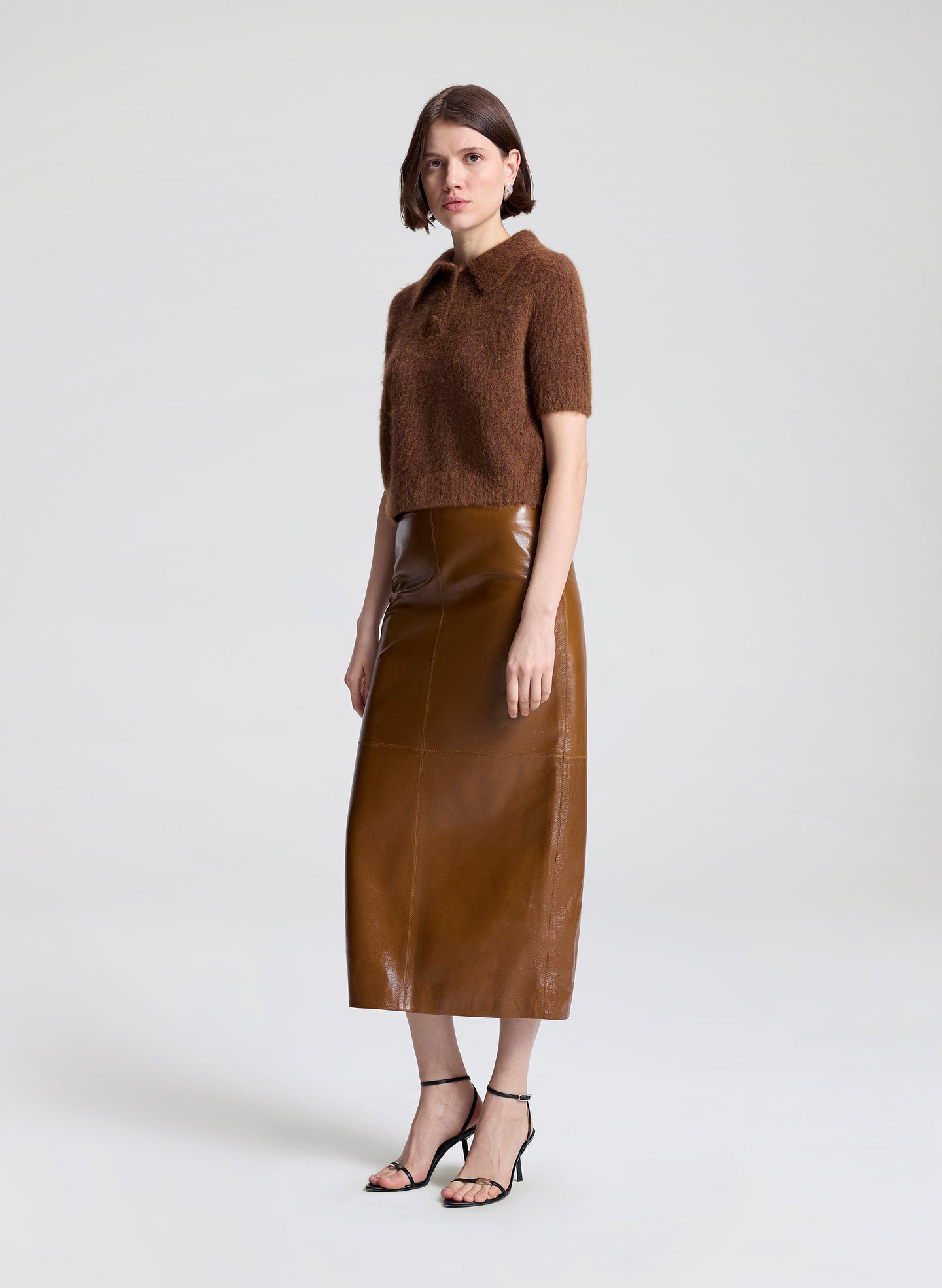 Woman wearing a brown knit top and leather skirt on a white background