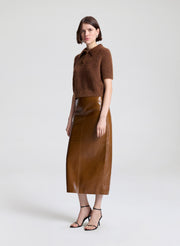 Woman wearing a brown knit top and leather skirt on a white background