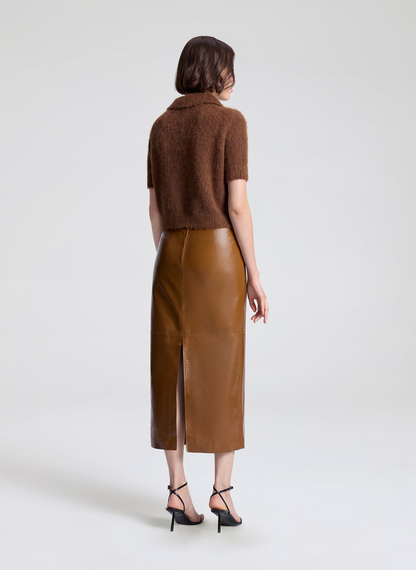 Woman wearing a brown knit top and leather skirt on a white background