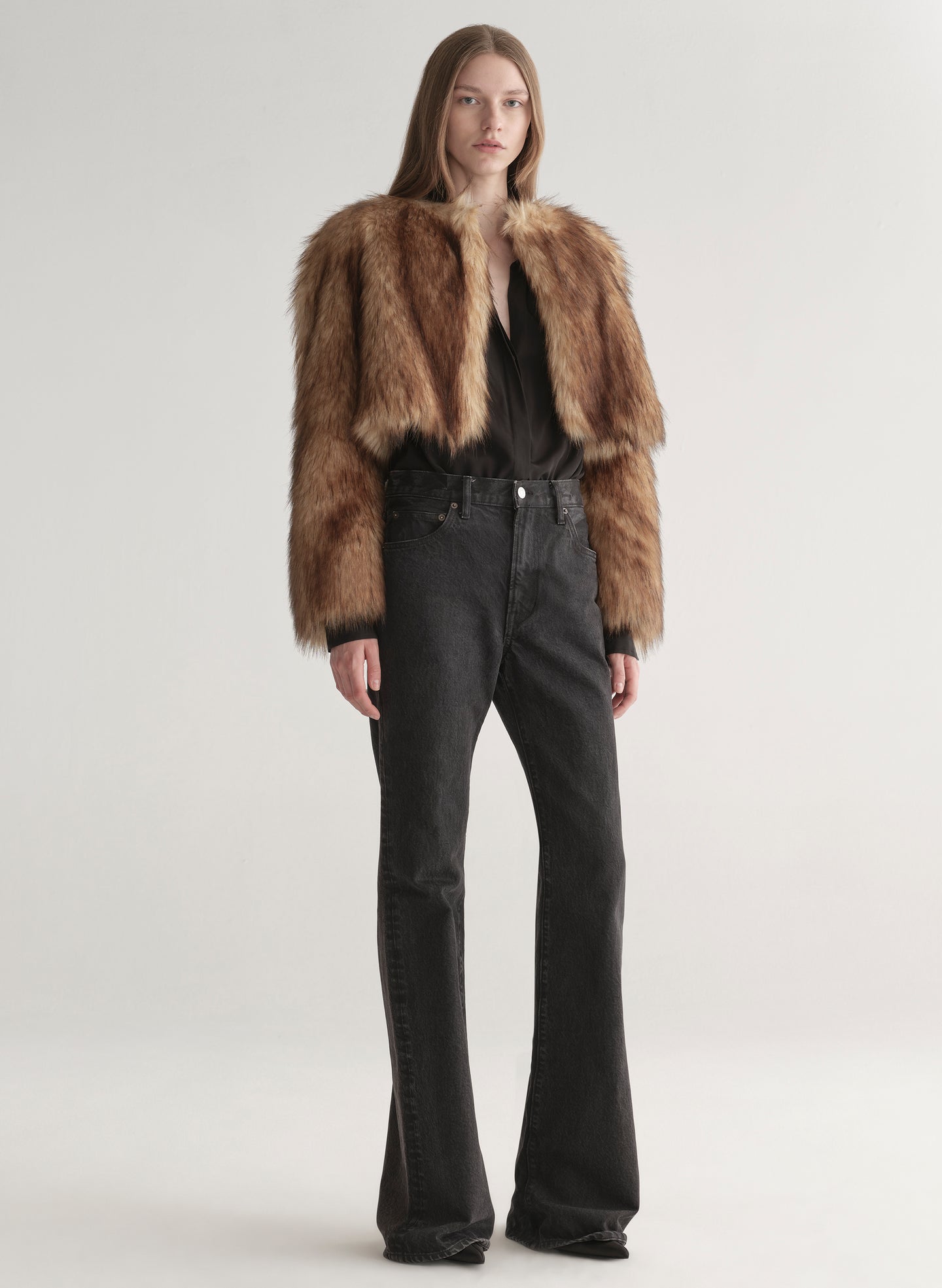 Woman wearing a brown faux fur coat over a black outfit on a plain background