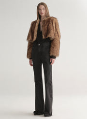 Woman wearing a brown faux fur coat over a black outfit on a plain background