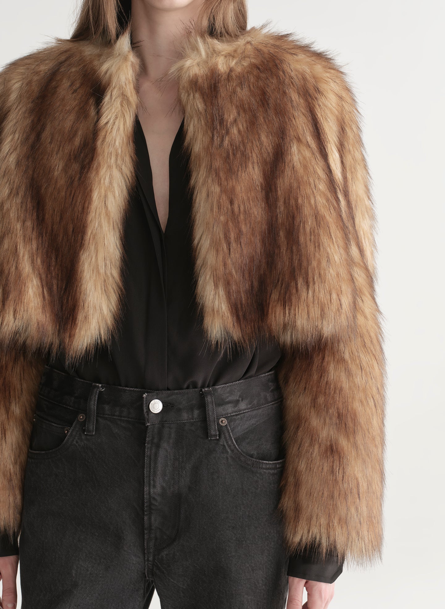 Woman wearing a brown faux fur coat over a black outfit on a plain background