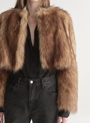 Woman wearing a brown faux fur coat over a black outfit on a plain background