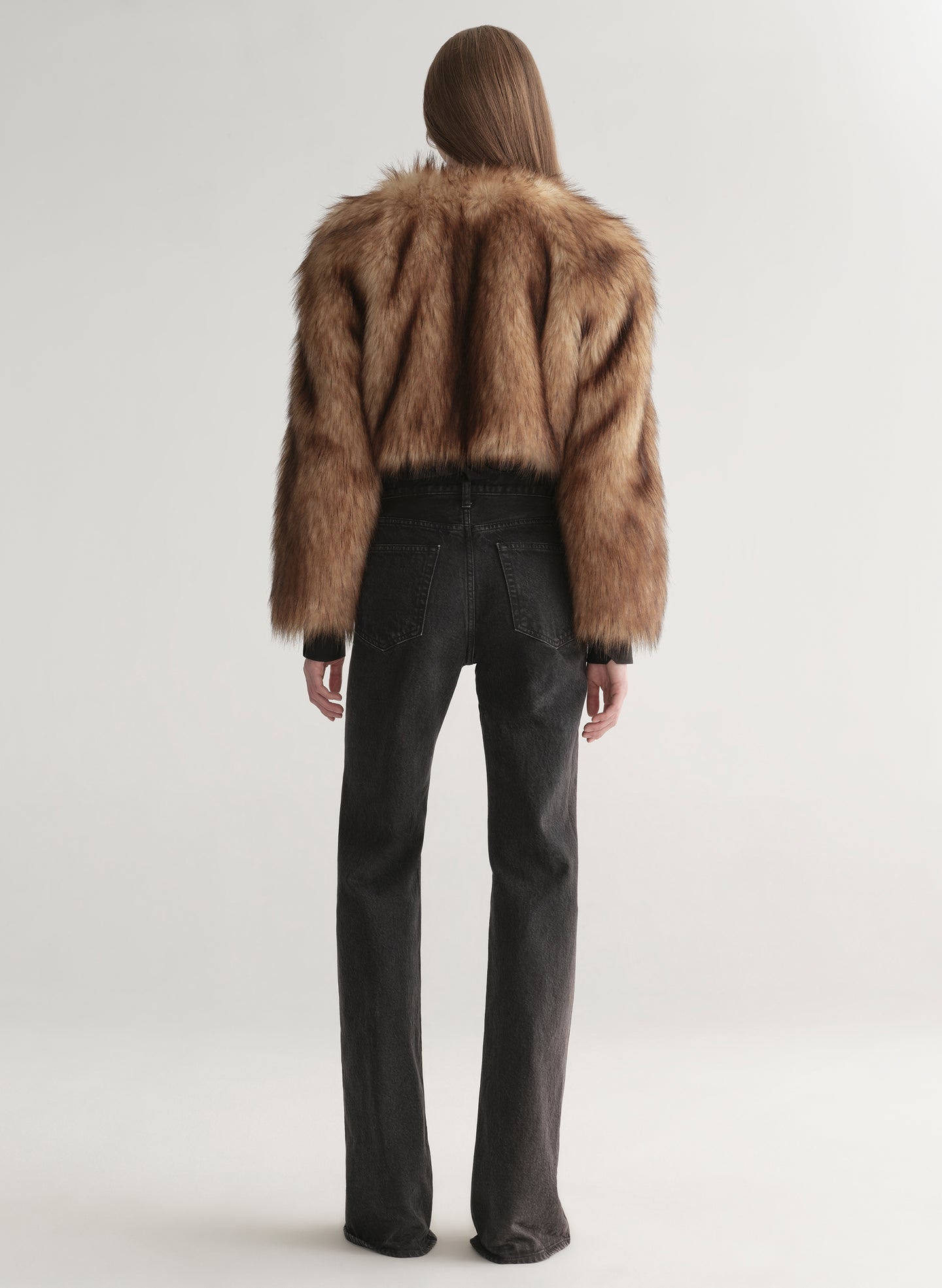 Woman wearing a brown faux fur coat over a black outfit on a plain background