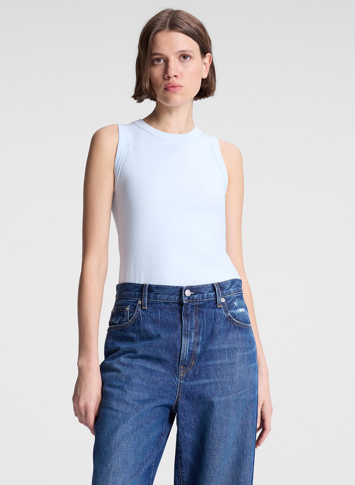 woman wearing light blue tank top and dark blue denim wide leg jeans