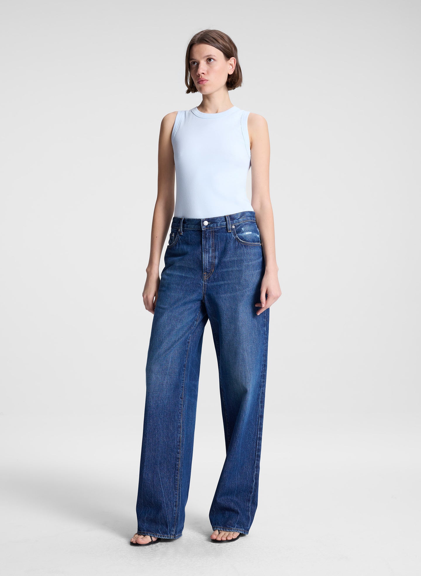 woman wearing light blue tank top and dark blue denim wide leg jeans