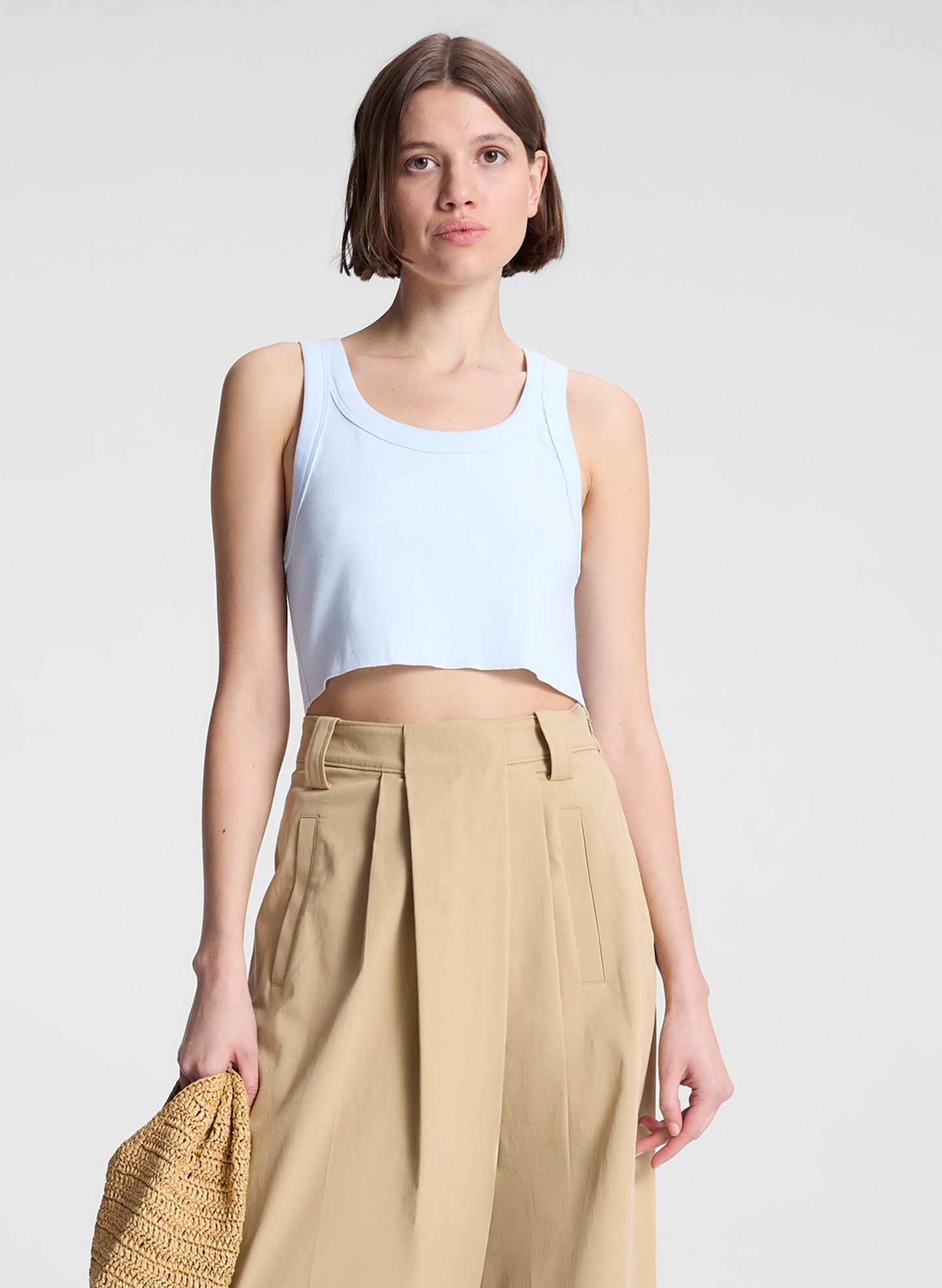woman wearing light blue cropped tank top and beige draped pants