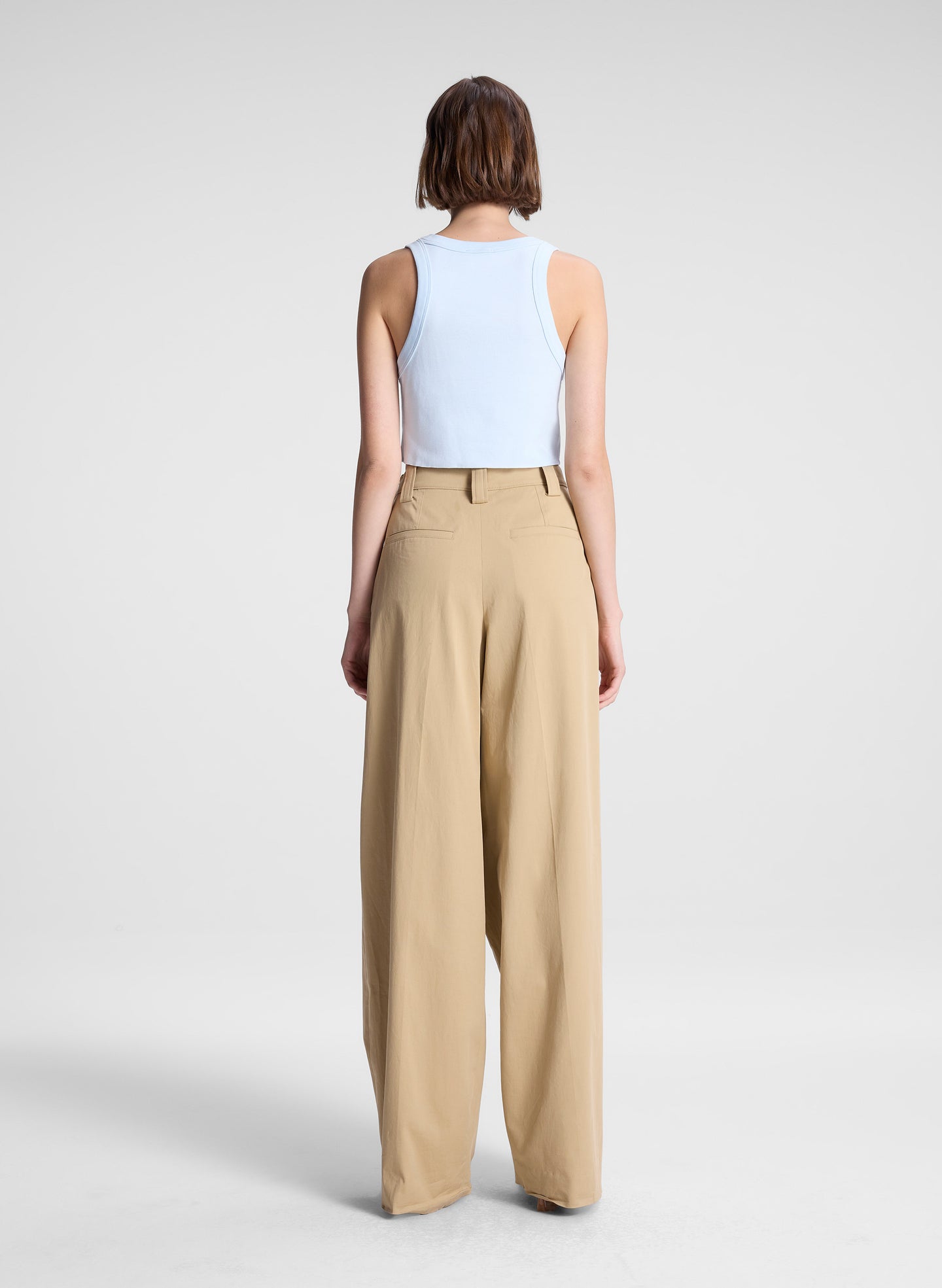 woman wearing light blue cropped tank top and beige draped pants