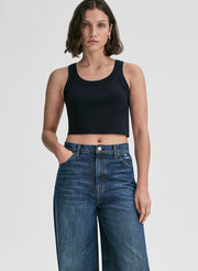 Woman wearing a navy blue tank top and blue jeans on a plain background
