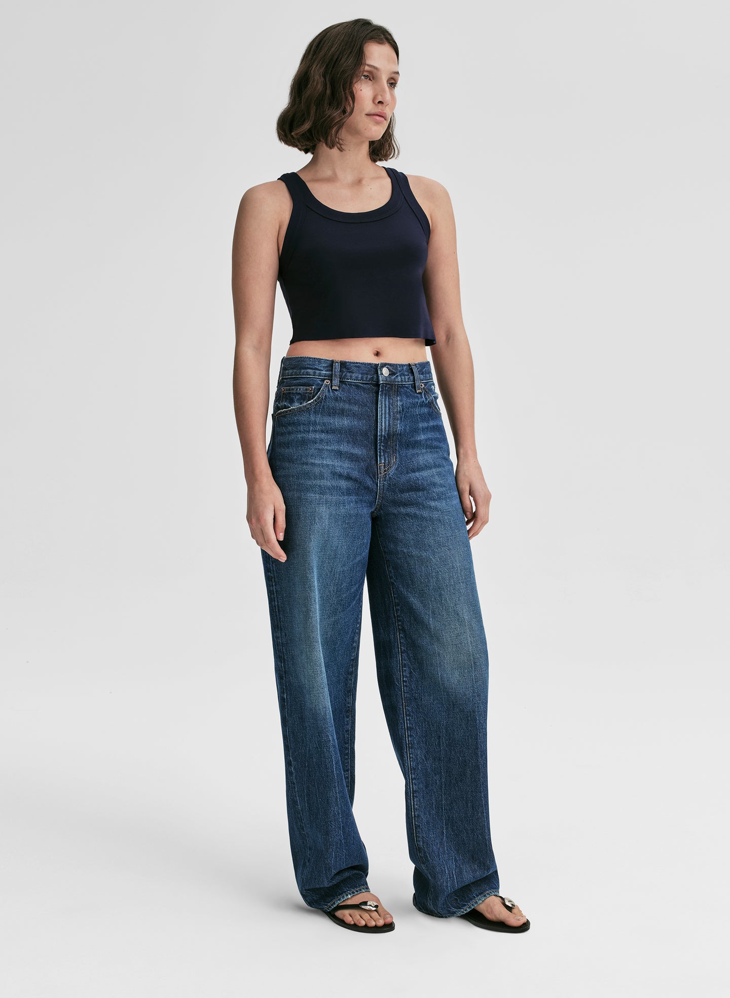 Woman wearing a navy blue tank top and blue jeans on a plain background
