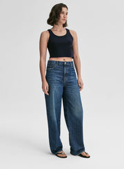Woman wearing a navy blue tank top and blue jeans on a plain background