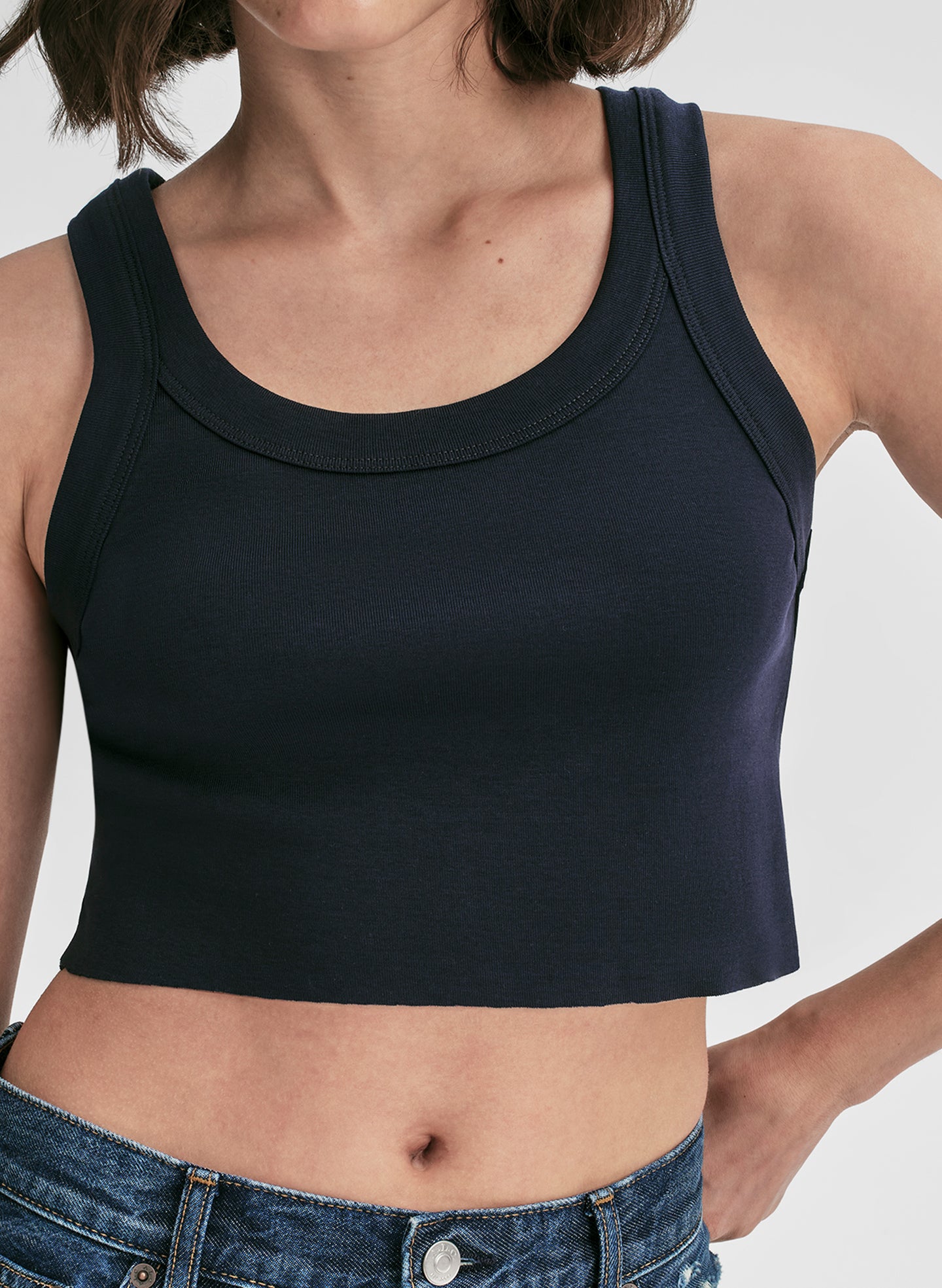 Woman wearing a navy blue tank top and blue jeans on a plain background