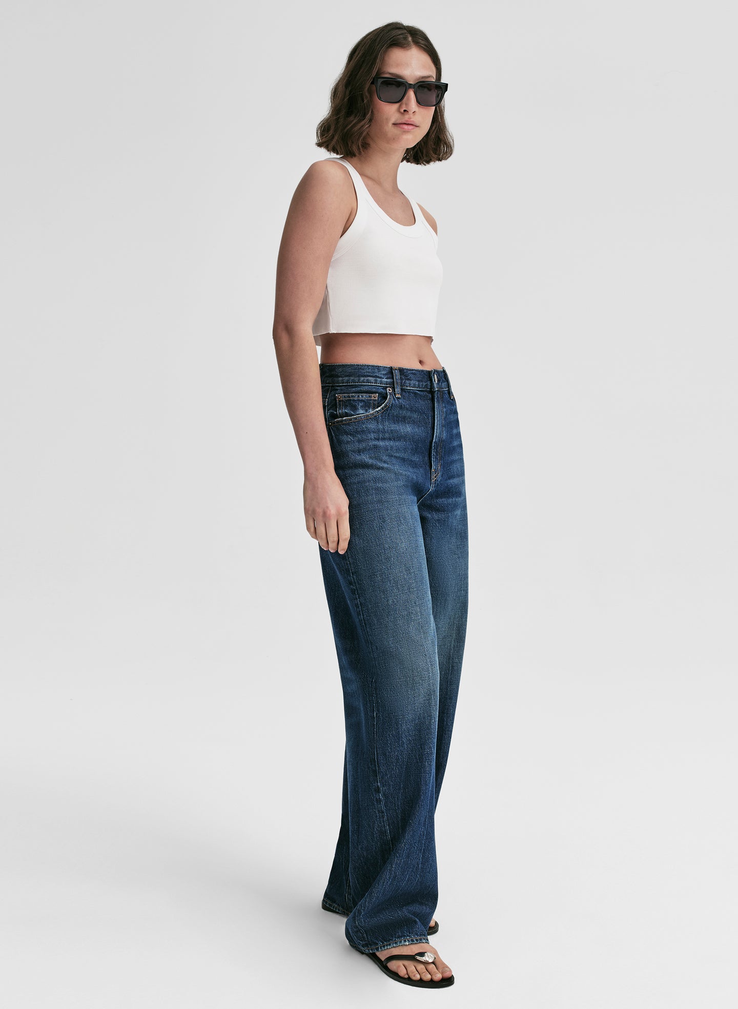 Woman wearing a white top and blue jeans on a plain background