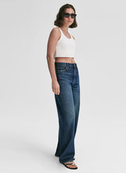 Woman wearing a white top and blue jeans on a plain background