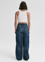 Person wearing blue jeans and a white top on a plain background