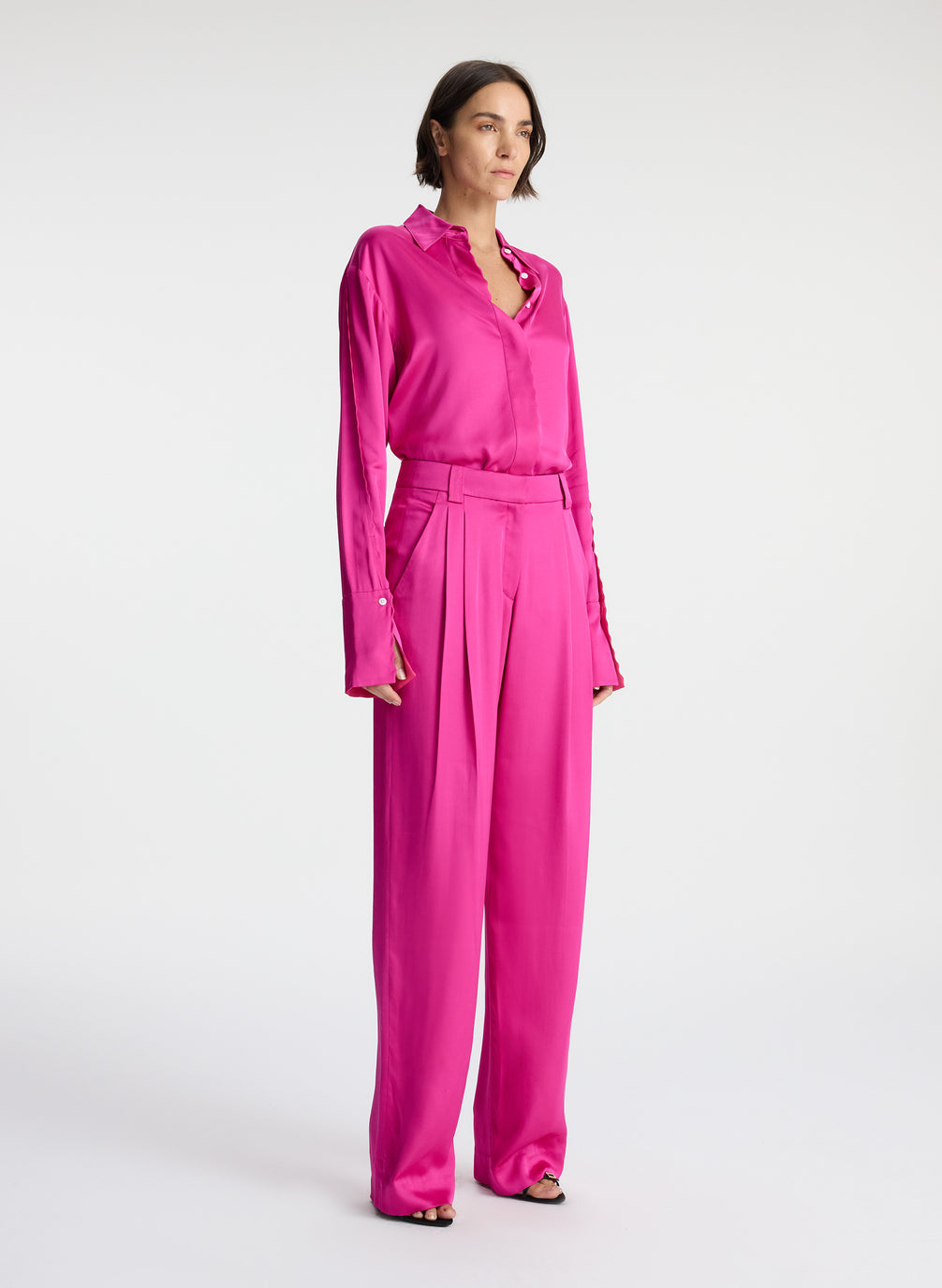 side view of woman wearing bright pink scalloped detailed long sleeve satin shirt and bright pink pants