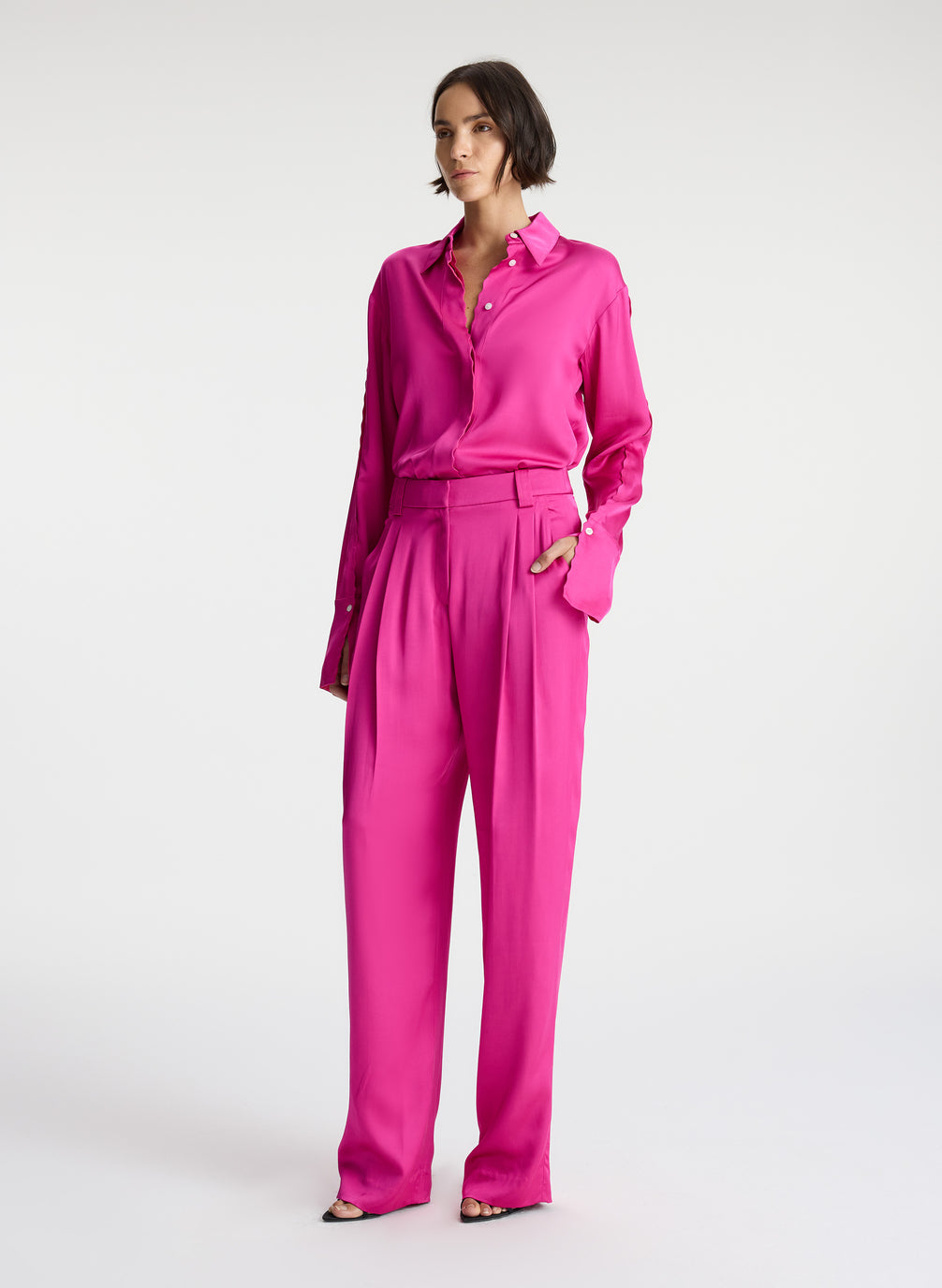 side view of woman wearing pink button down collared satin long sleeve shirt with matching pink satin pants
