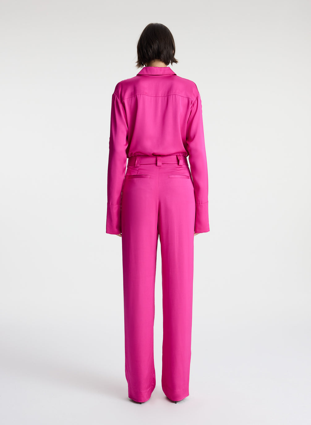 back view of woman wearing bright pink scalloped detailed long sleeve satin shirt and bright pink pants